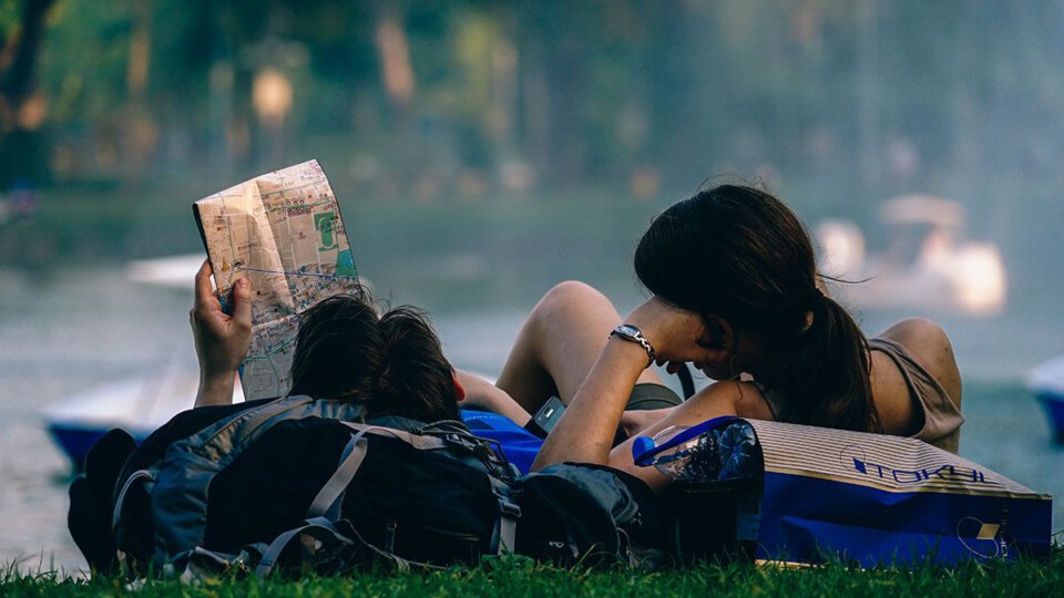 Ein Pärchen liegt in einem Park. An ihrem Reiserucksack gelehnt studieren sie einen Stadtplan.